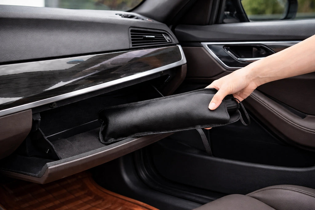 Hand placing folded black umbrella-style car sunshade into vehicle glove compartment for compact storage.