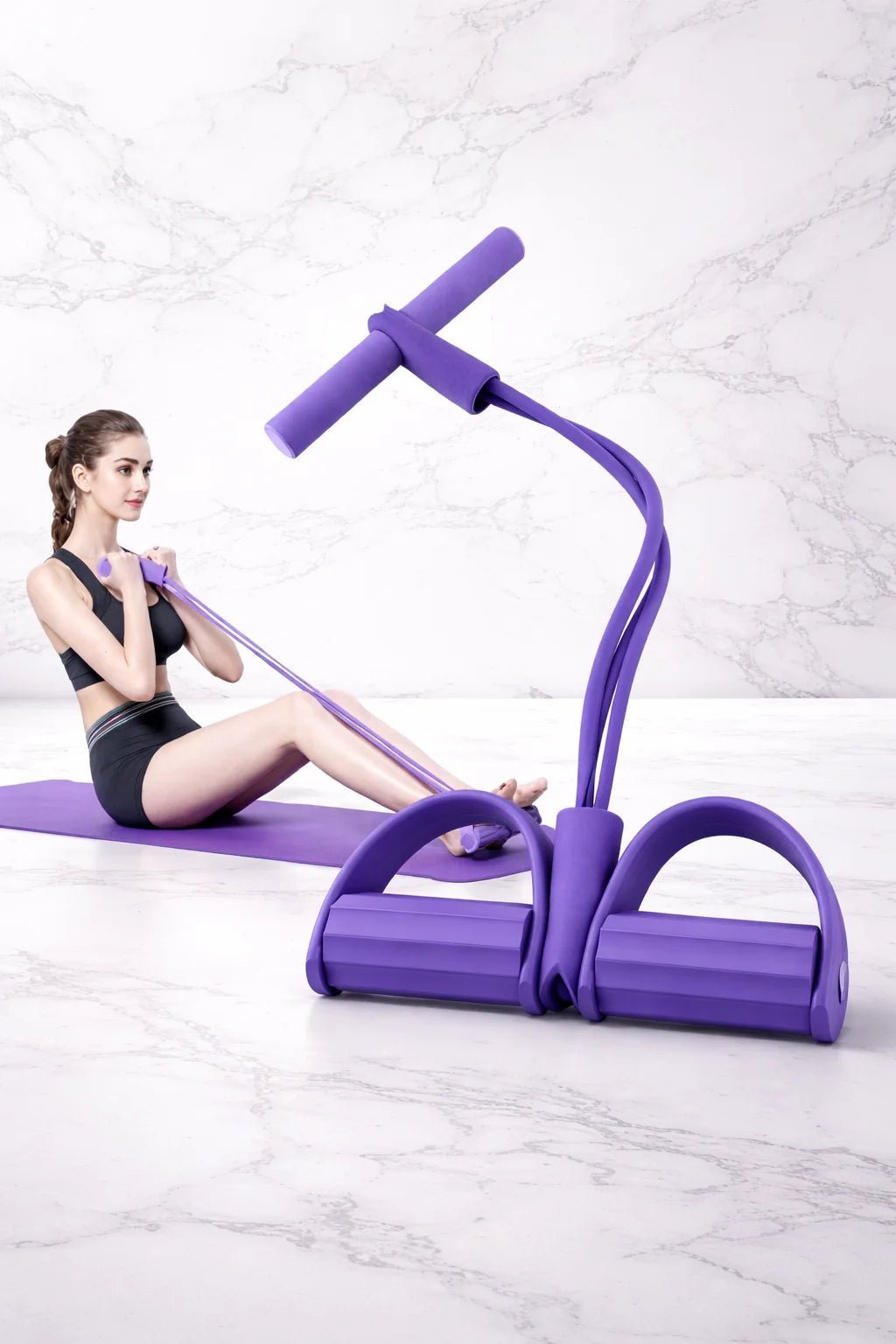 Woman using purple pedal resistance band with cushioned grips and foot pedals for seated full-body workouts at home